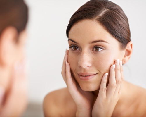 A gorgeous young woman looking at her reflection in the mirror with her hands on her face